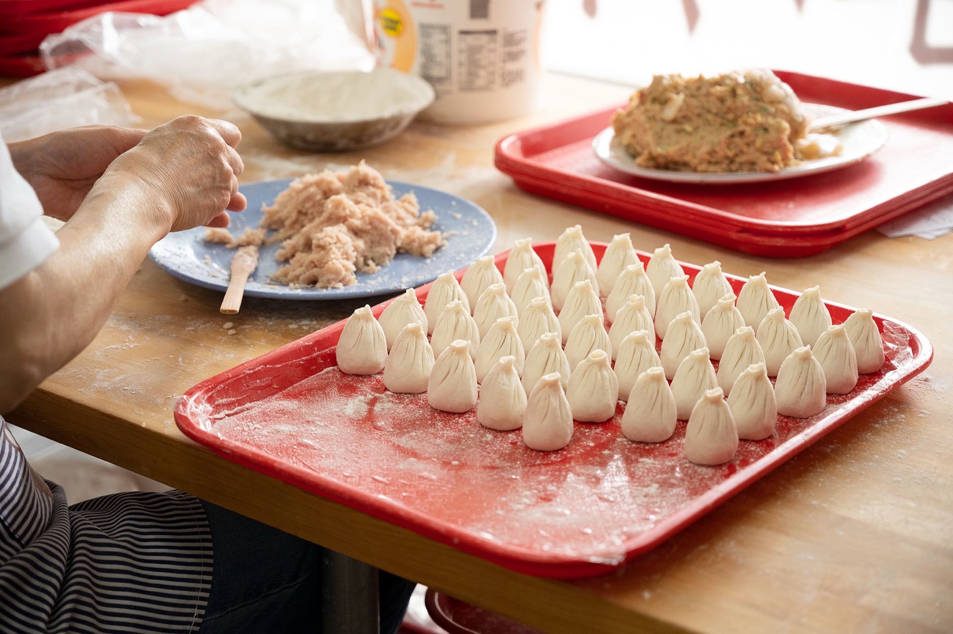 Neatly arranged rows of hand-folded xiaolongbao on a flour-dusted red tray