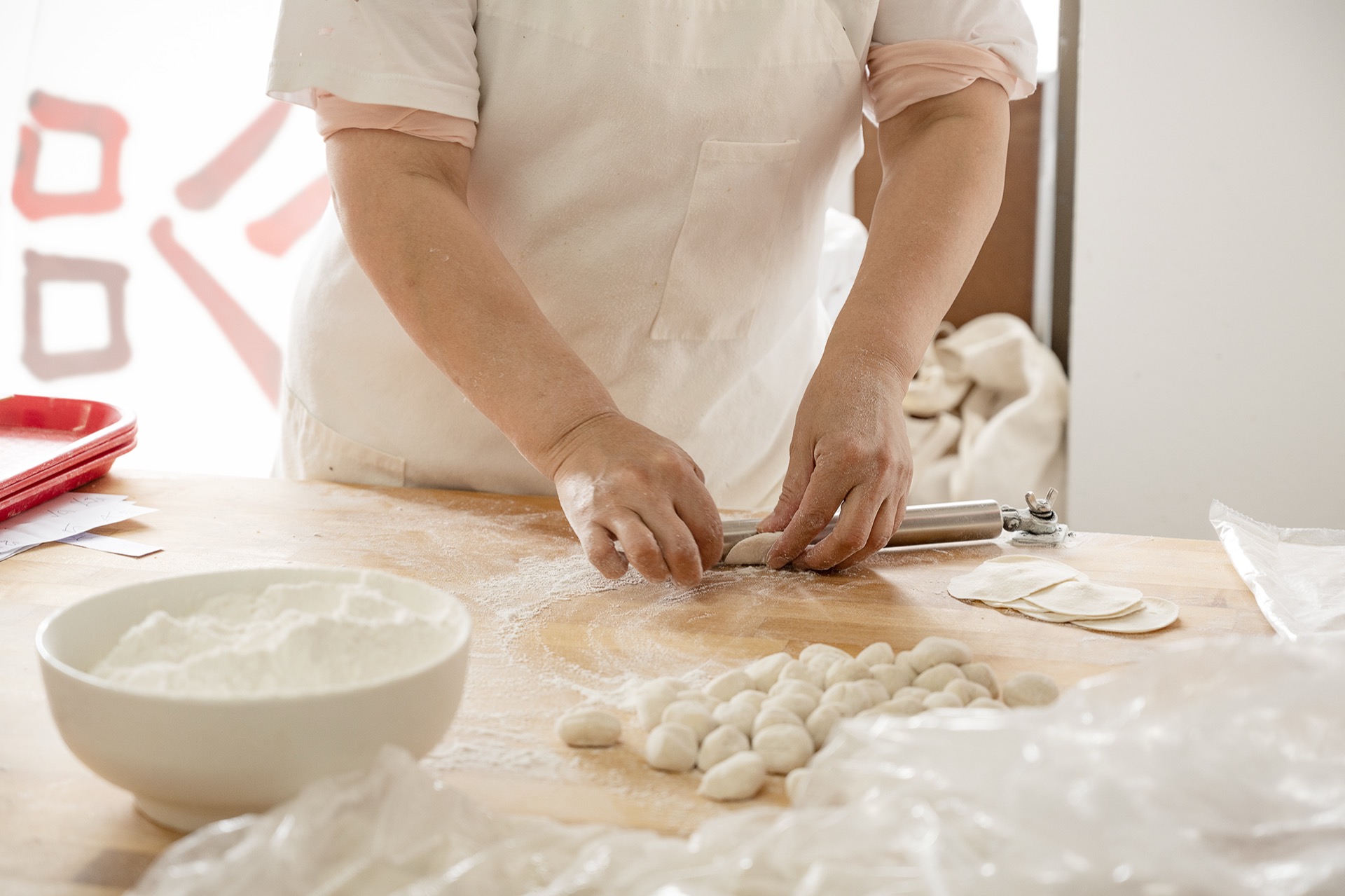 Chef rolling out dumpling wrappers by hand with a metal rolling pin