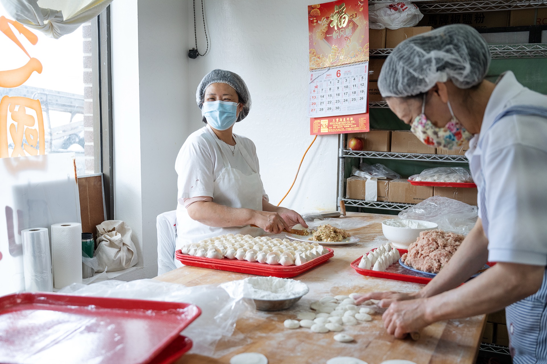 Two dumpling makers rolling wrappers and filling dumplings side by side