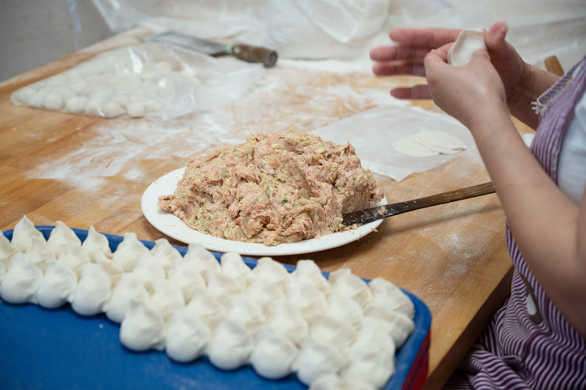Hands folding dumplings beside a plate of seasoned filling