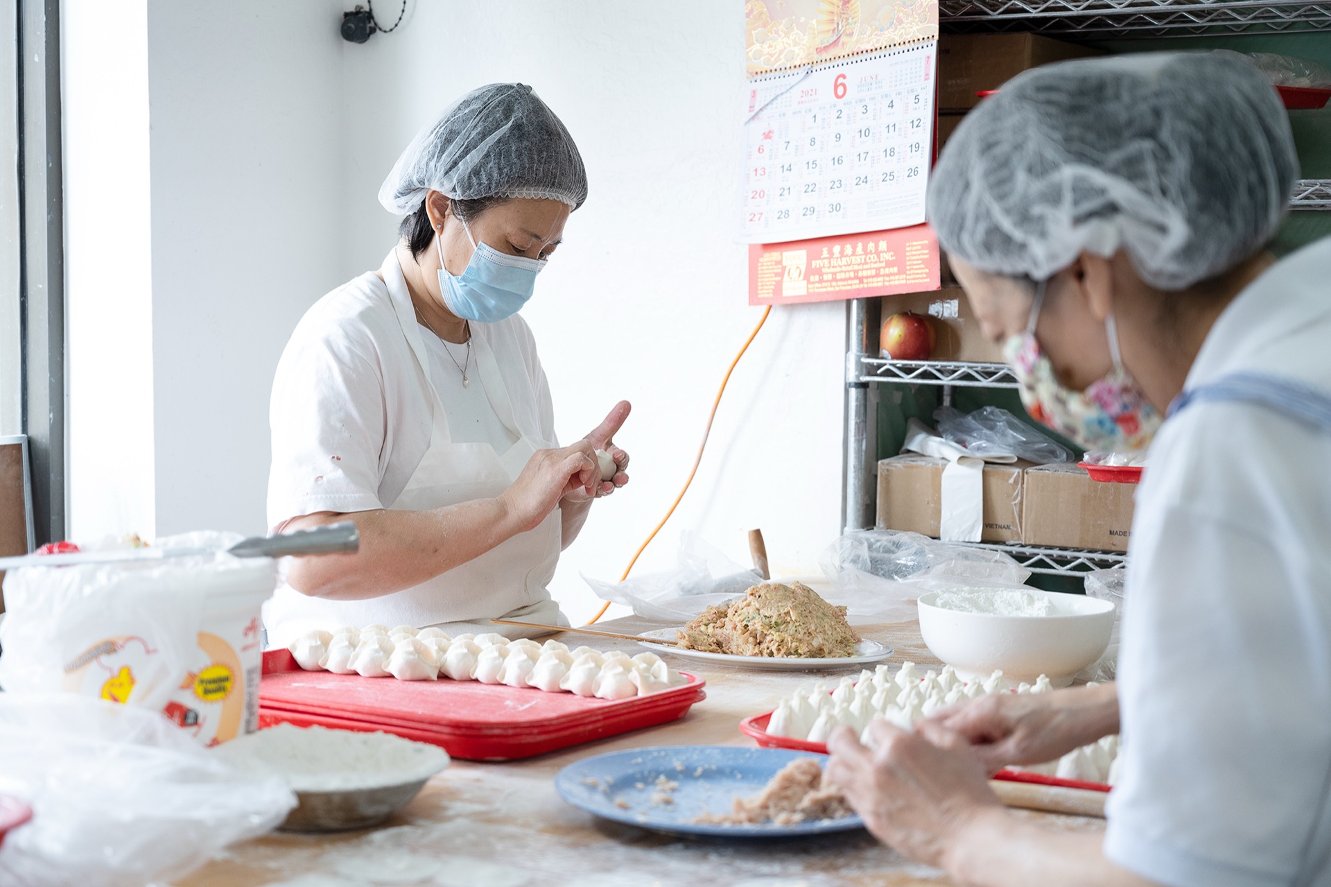 Two kitchen staff wrapping dumplings together at a worktable
