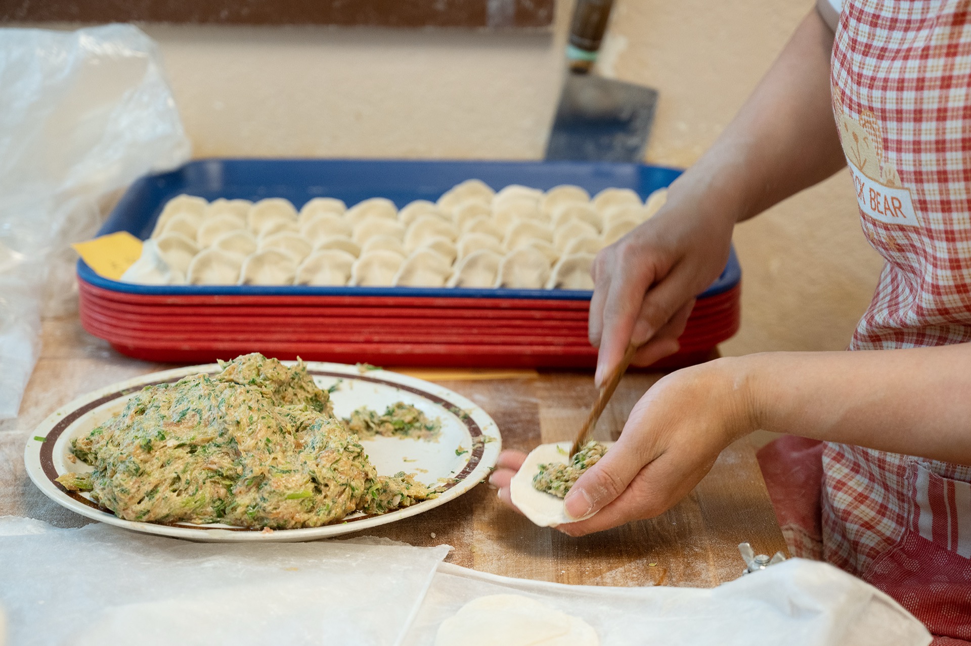 Hand-filling dumplings with chopsticks from a plate of seasoned filling
