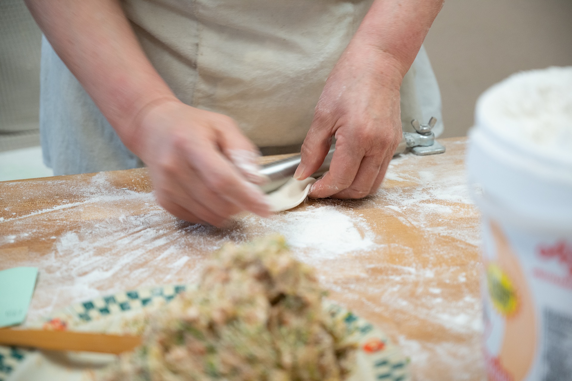 Hands using a rolling pin to flatten dough into a thin dumpling wrapper