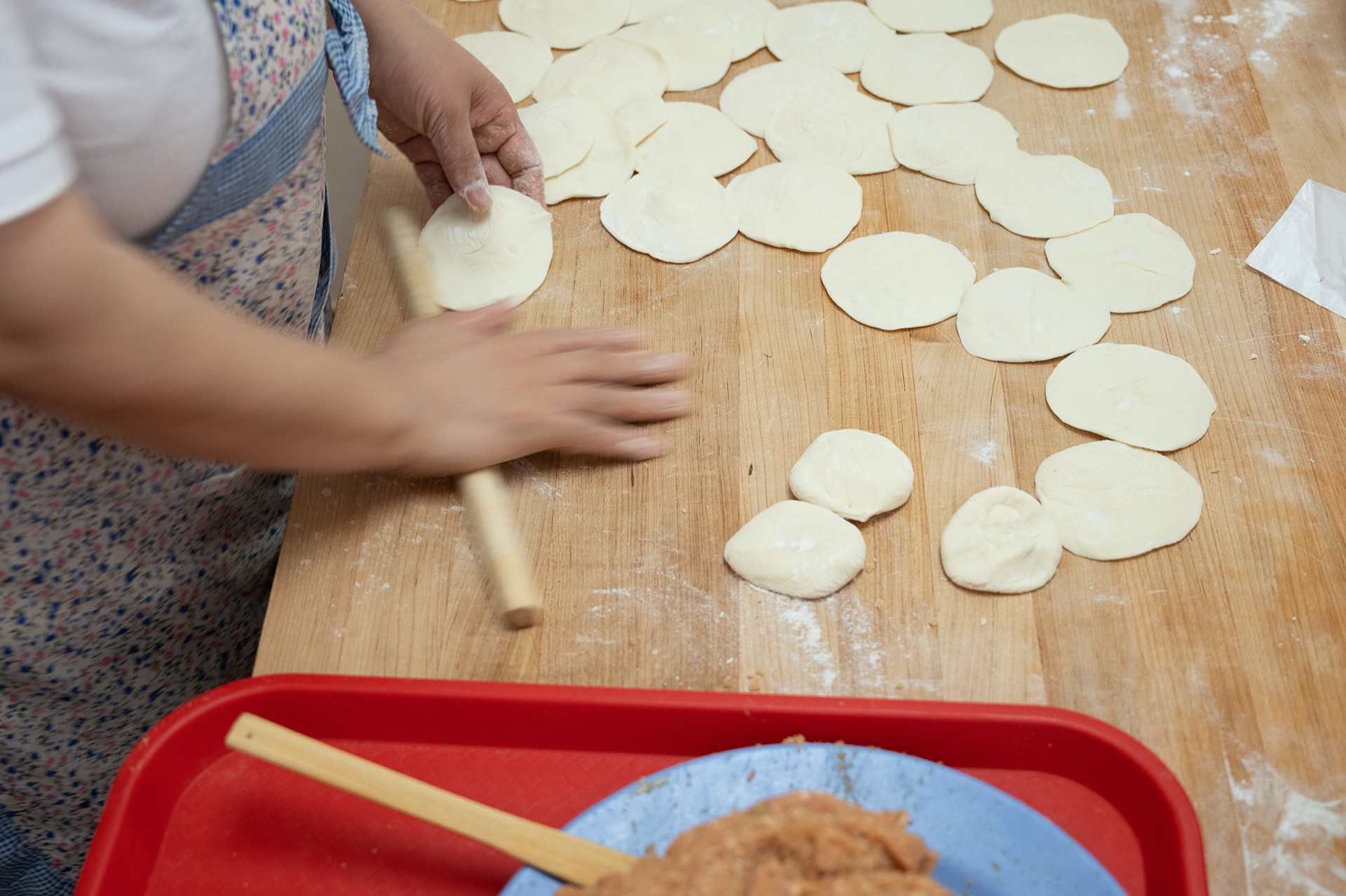 Hands rapidly rolling dumpling wrappers with a wooden rolling pin