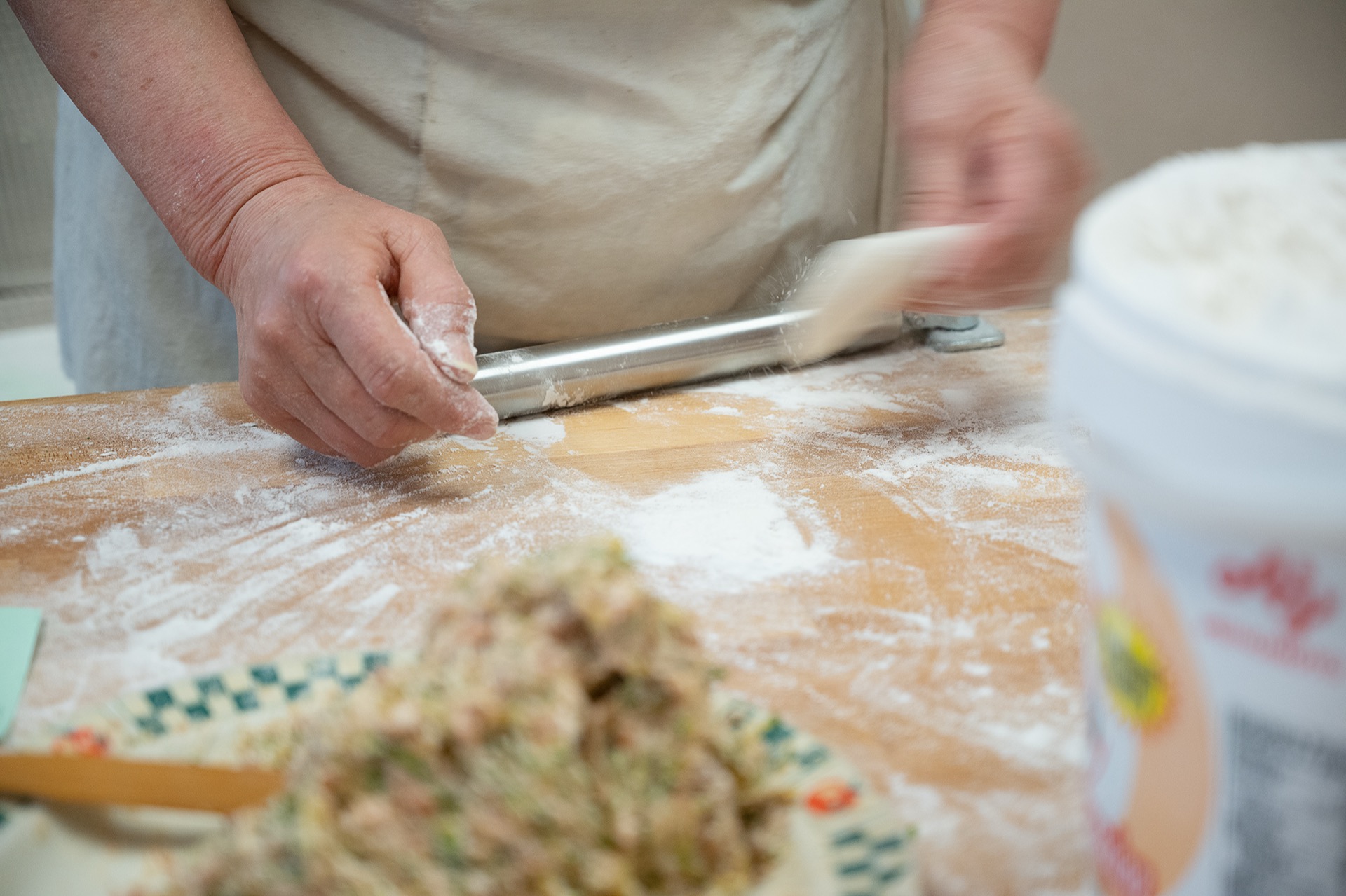 Close-up of hands rolling dough with a metal rolling pin