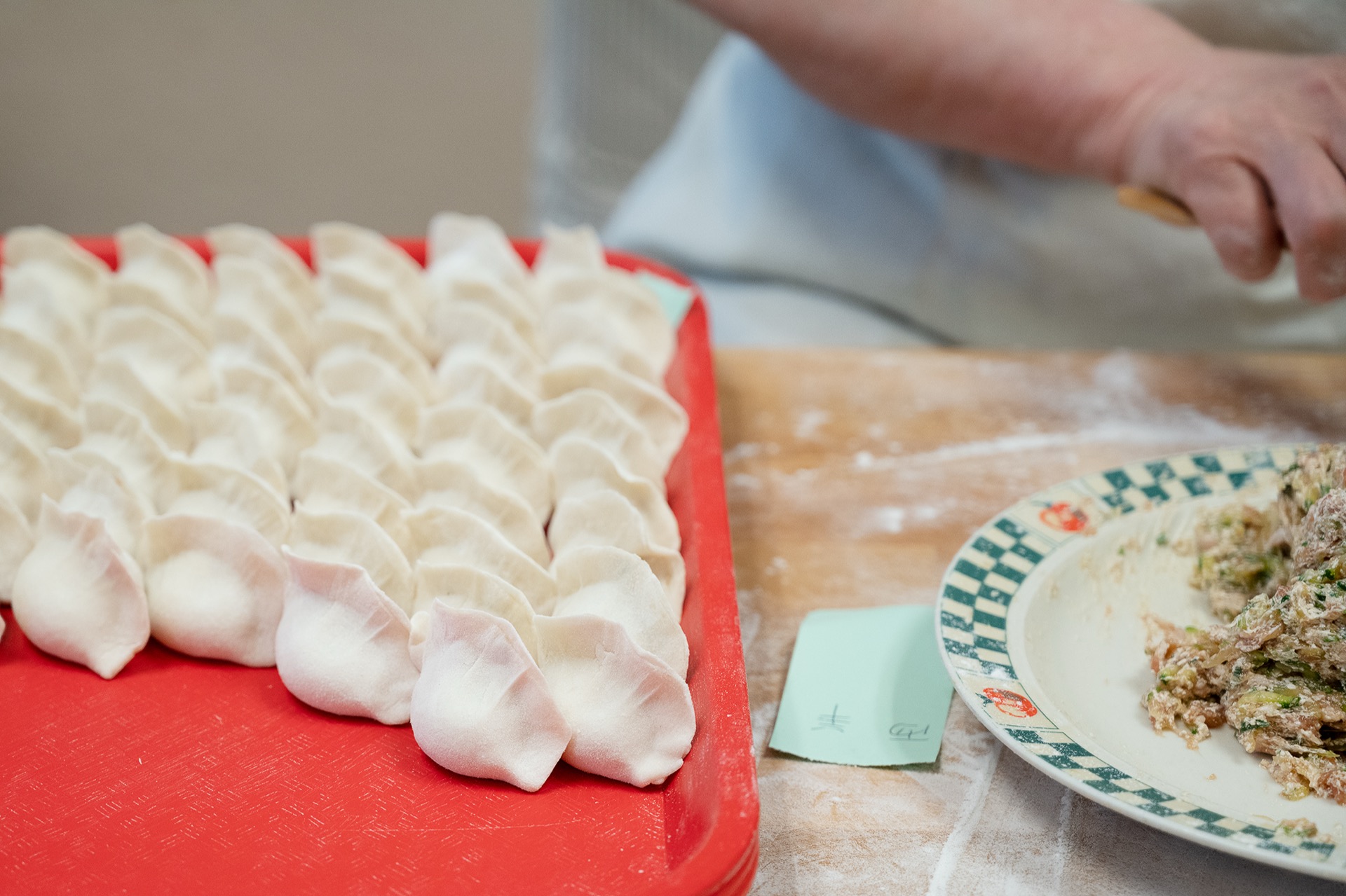 Red tray filled with rows of neatly pleated uncooked Chinese dumplings